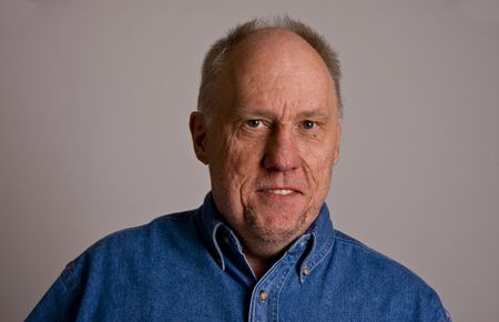 An older bald man in a blue shirt on a grey backgroundの写真素材