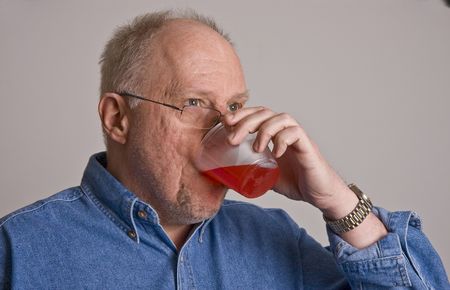 An older bald man in a blue denim shirt on a grey background wearing glasses and drinking from a plastic cupの写真素材