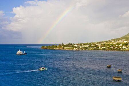Ships sailing around a green tropical island with a rainbow in the skyの写真素材
