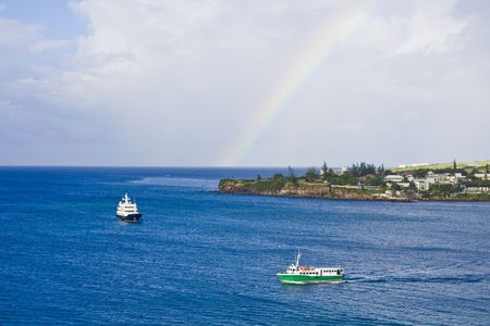 Blue and green ferry boats cruising past island with a rainbowの写真素材