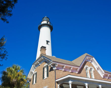 A white lighthouse rising from behind a brick houseの写真素材