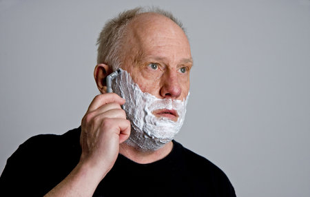An older bald man in a black shirt shaving