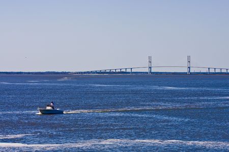A suspension bridge over a channel in the bay with a fishing boatの写真素材