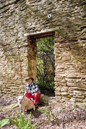 Hispanic Man in plaid shirt and orange pants with a dog by an old rock wallの写真素材