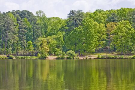 A peaceful lake and green trees and an old iron bridgeの写真素材
