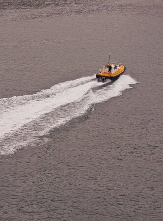 A yellow and black pilot boat speeding across a calm bayの写真素材