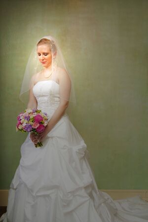 A bride in a white bridal gown looking down at her bouquetの写真素材
