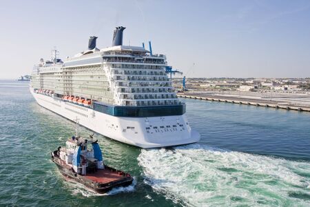 A luxury cruise ship followed by a tugboat in a busy portの写真素材