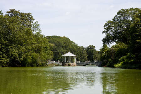 A stone gazebo and walkway across a calm green lakeの写真素材