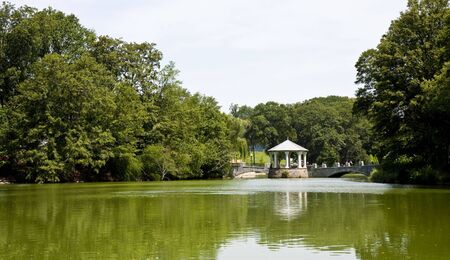 A stone gazebo and walkway across a calm green lakeの写真素材