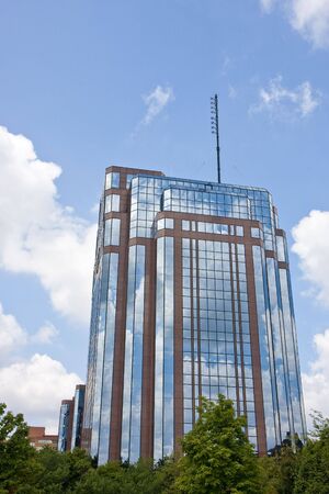 A modern red brick and blue glass office tower reflecting sky and cloudsの写真素材