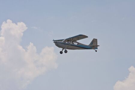 A blue and white single prop plane flying against a blue skyの写真素材