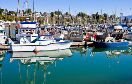 A blue and white fishing boat at a busy harbor on calm blue waterの写真素材