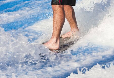 Bare legs of a man on a surf board in blue and white waterの写真素材