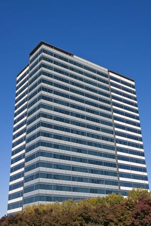A modern blue and white office tower rising from trees into a blue skyの写真素材