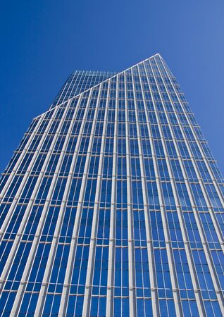 A modern blue glass office building with a pointed top rising into a clear blue skyの写真素材