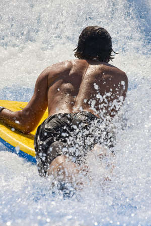 A man on a yellow surfboard from the backの写真素材