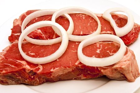 Two fresh strip steaks on a white plate with  sliced onion ringsの写真素材