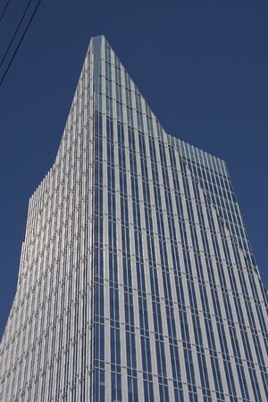 A modern blue and silver office tower rising to a pyramid top in blue skyの写真素材