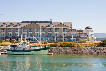 A green fishing boat docked by a hotel on the waterの写真素材