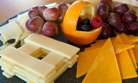 Sliced cheeses and grapes on a tray with an orange basketの写真素材