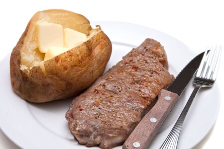 A strip steak and a potato with butter with knife and fork on a white plateの写真素材