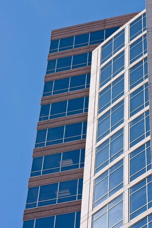 Two buildings with blue glass windows on blue skyの写真素材