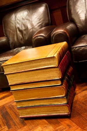 A stack of old books on a floor by leather chairsの写真素材