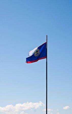 The flag of Belize blowing in the wind against a blue skyの写真素材
