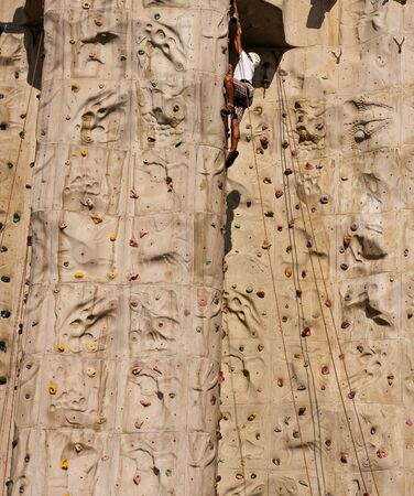A climber at the top of a rock climbing wallの写真素材