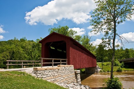 An old red covered bridge b y a stone wall under nice skyの写真素材