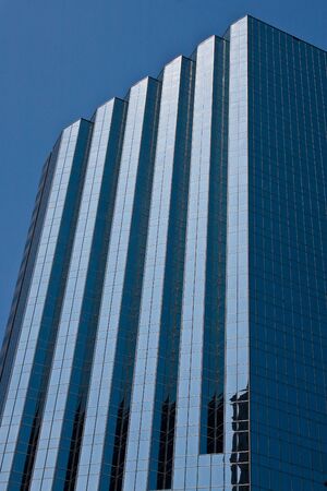 A blue angled glass office tower rising into a clear blue skyの写真素材