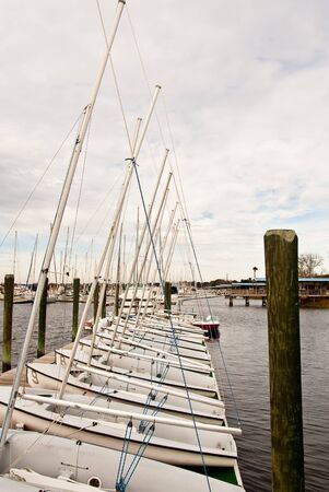 A row of small identical sailboats at a pier under cloudy skiesの写真素材