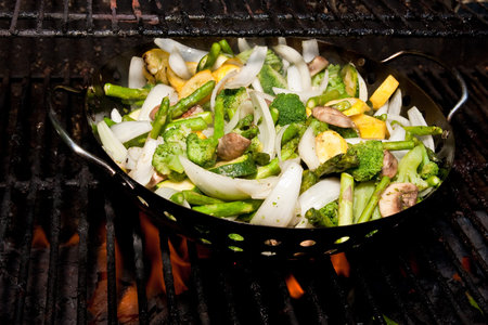 Fresh cut vegetables in a pan roasting over an open fire on a grillの写真素材