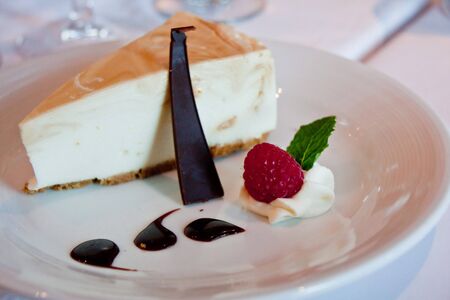 A slice of cheesecake on a plate with chocolate and raspberryの写真素材