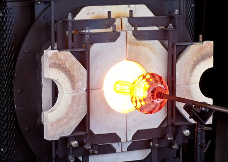 A glass blower turning a vase on a rod in a hot ovenの写真素材