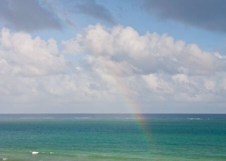 Stormy skies over a green sea with rainbow in foregroundの写真素材