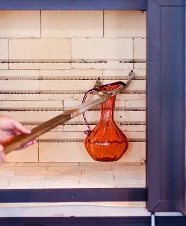 A glass blower putting an orange pitcher in an anealling oven to cool