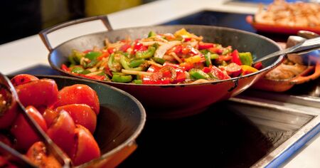 Vegetables cooking in woks at restaurantの写真素材