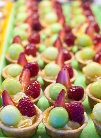 A tray of fresh green and red fruit pastries on a buffetの写真素材