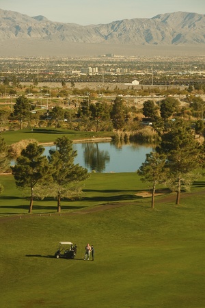 Two golfers by a cart on a green by a calm lakeの写真素材