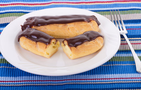 Two chocolate covered eclairs on a white plate and colorful placemat