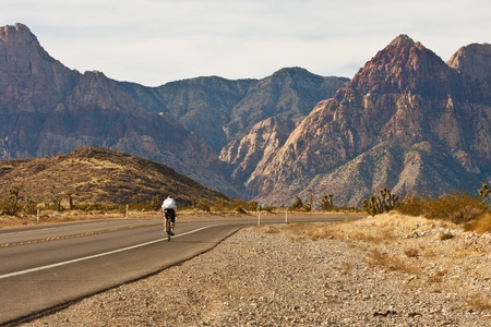 A lone cyclist peddling up a desert highway toward distance mountainsの写真素材