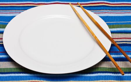 An empty white plate on a colorful placemat with a pair of chopsticksの写真素材