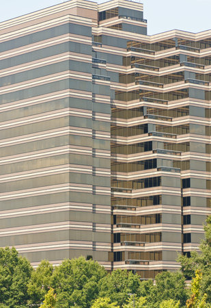 A modern glass office tower rising out of green trees