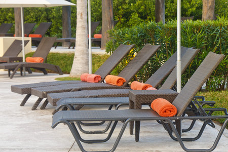 Row of brown chaise lounges on patio with orange beach towels