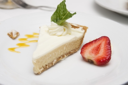 A slice of key lime pie on a plate garnished with a strawberry and mint leafの写真素材