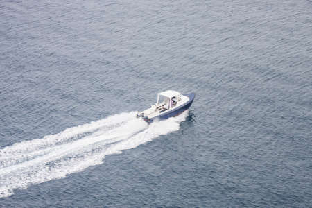 A small blue and white boat skimming across a calm blue bayのeditorial素材