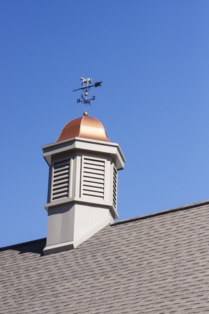 A cupola with copper roof and weather vane on a roof under a clear blue skyの写真素材