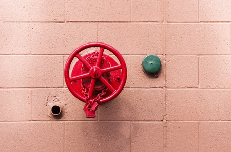 A red fire valve and green pipe cover on a red block wallの写真素材